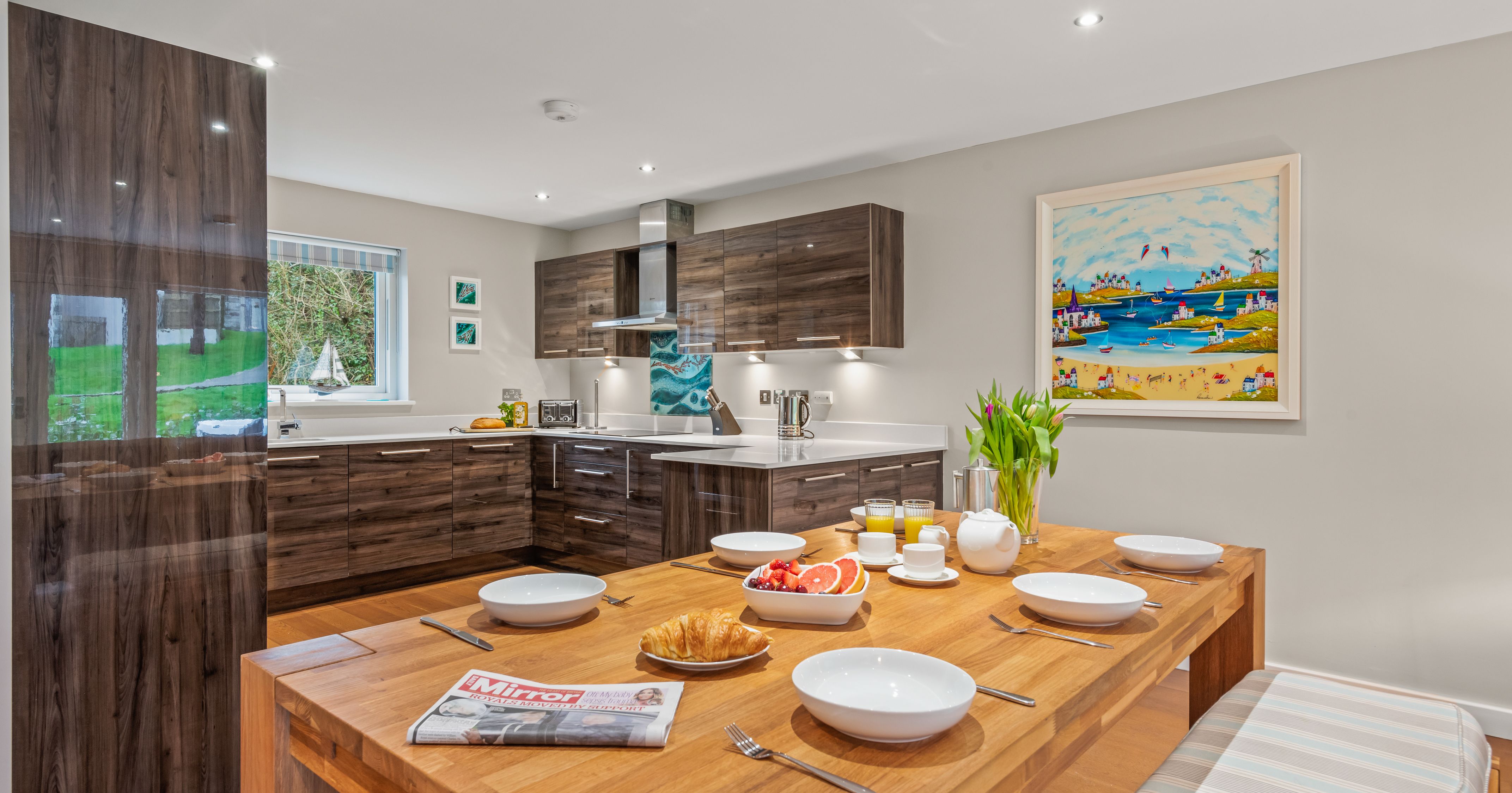 Modern kitchen and dining area with wooden cabinets and breakfast set on table.