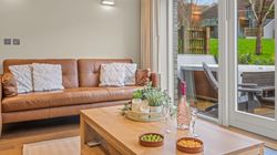 Modern living room with a brown leather sofa, large window doors, a wooden coffee table with snacks and drinks, and an outdoor hot tub view.