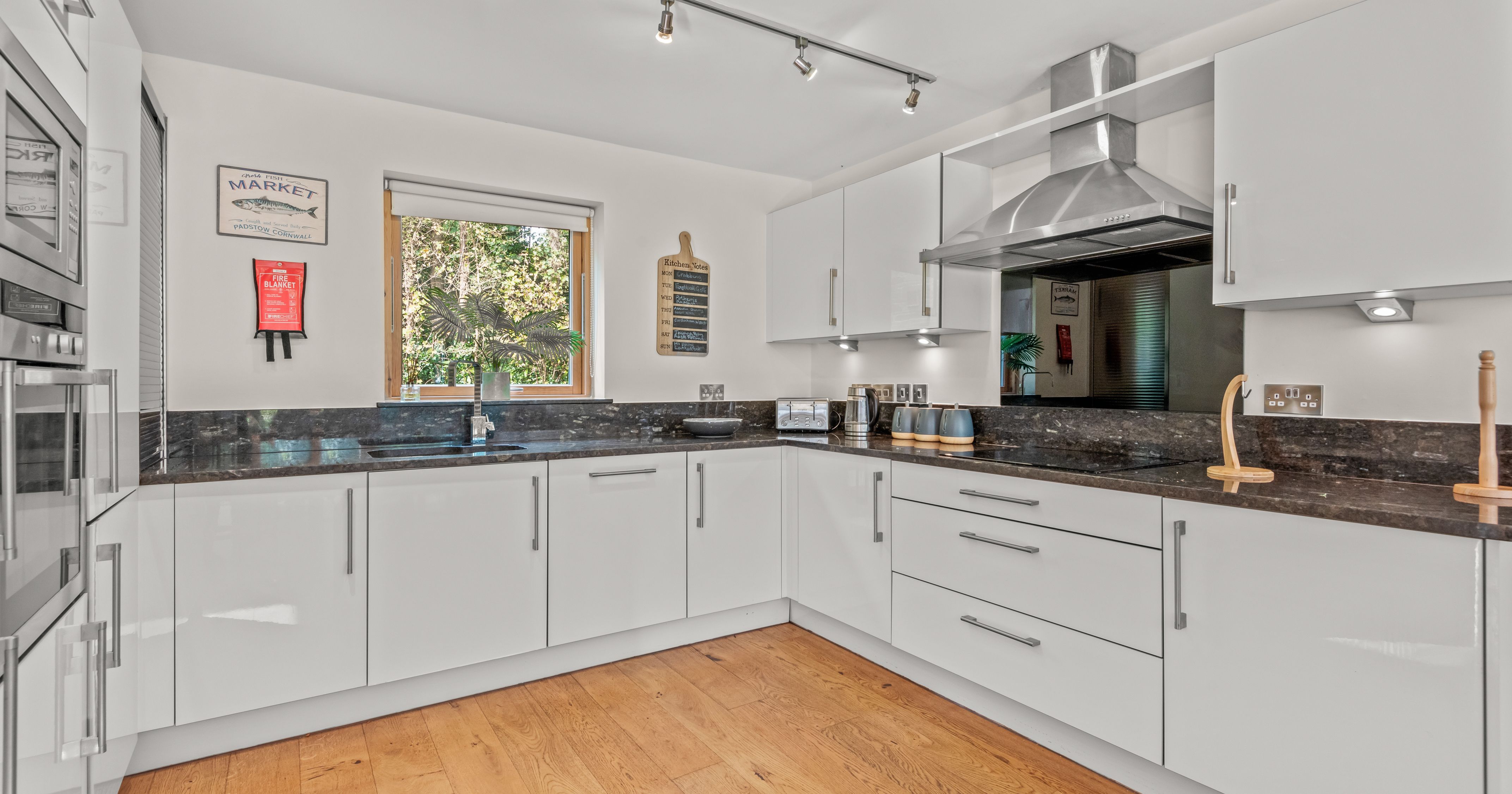 Modern kitchen with white cabinets, stainless steel appliances, and wooden floor.