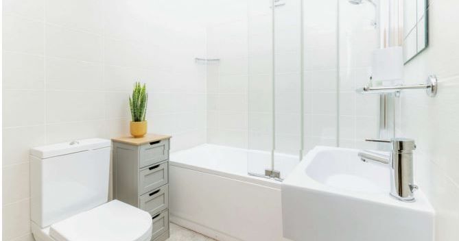 Modern bathroom with white fixtures, a bathtub, toilet, sink, and small cabinet with a potted plant.