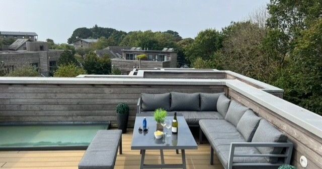 Modern rooftop terrace with outdoor seating and table, surrounded by trees and buildings.