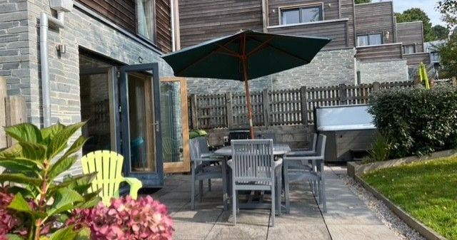 Modern townhouse patio with outdoor dining set, umbrella, hot tub, and blooming flowers.