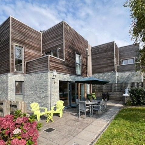 Modern house with wooden and stone exterior, patio seating and garden