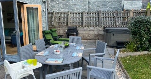 Patio with outdoor dining table, chairs, high chair, and hot tub in fenced backyard