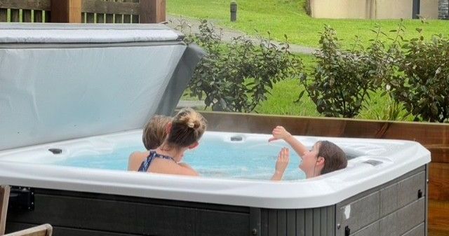Two people relaxing in a hot tub outdoors near some greenery.