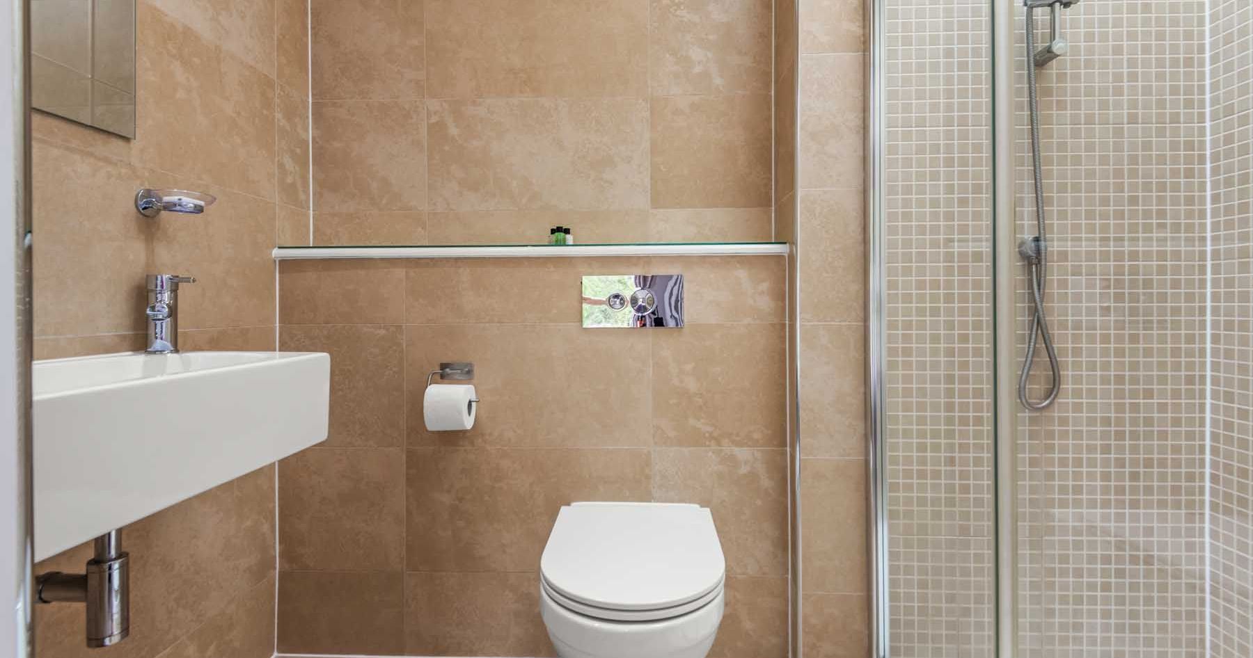 Modern bathroom with beige tiles, a toilet, sink, and glass shower enclosure