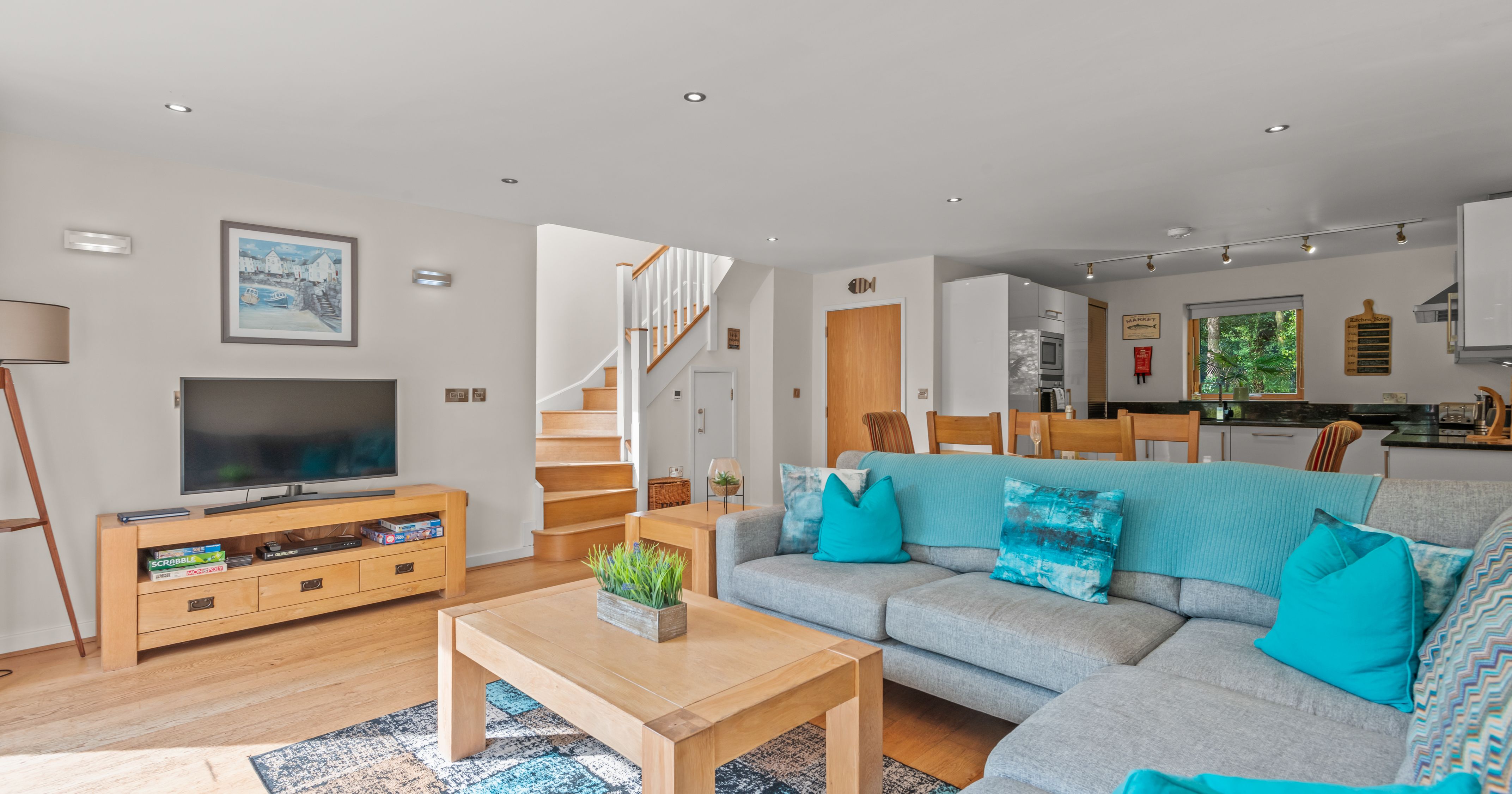 Modern open-plan living room and kitchen with light wood furniture and teal accents.