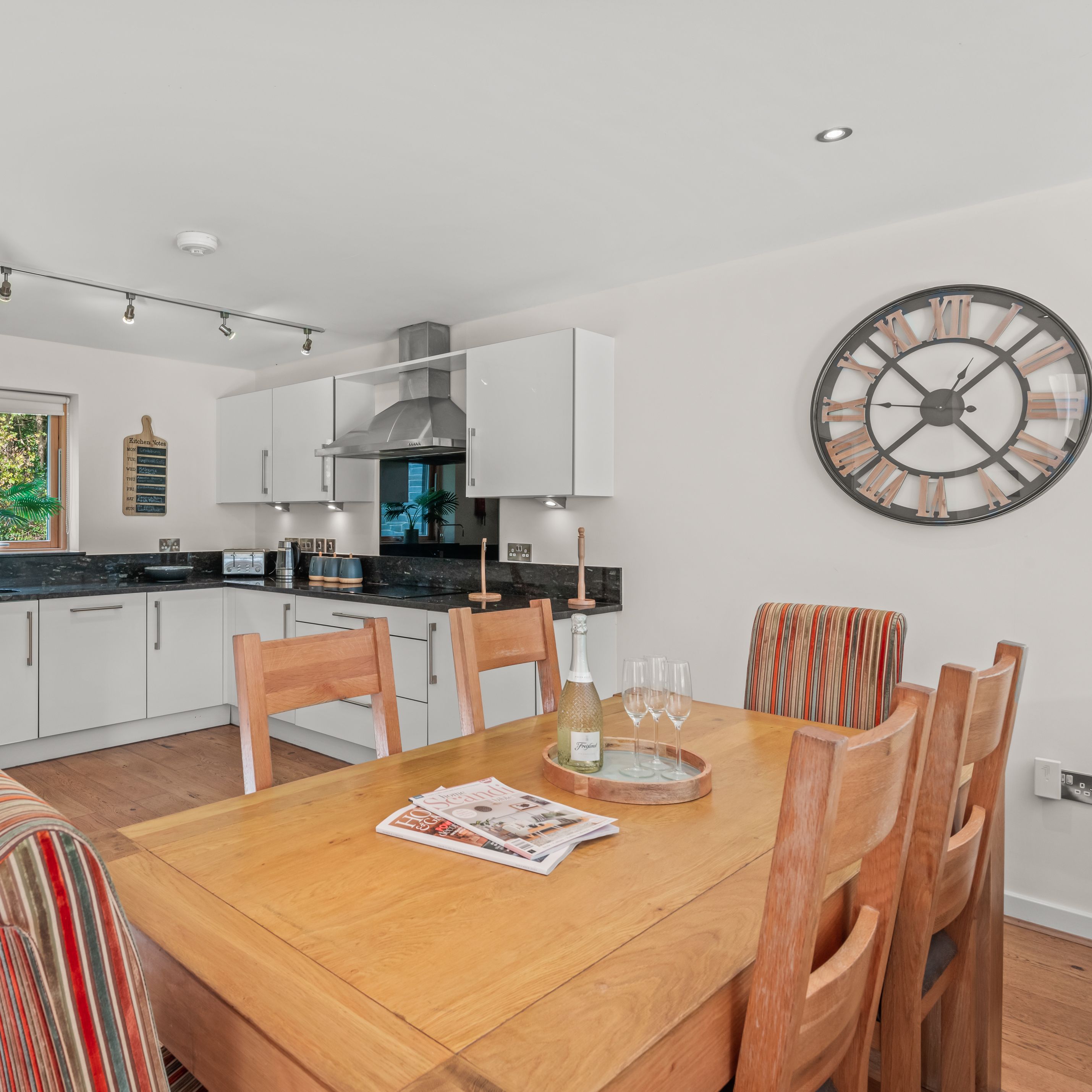 Modern kitchen and dining area with wooden table, striped chairs, and large wall clock