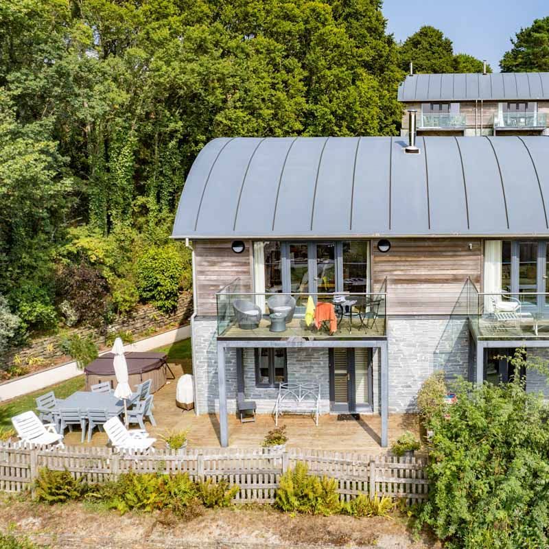 Modern house with curved metal roof, glass balconies, and patio in a wooded setting