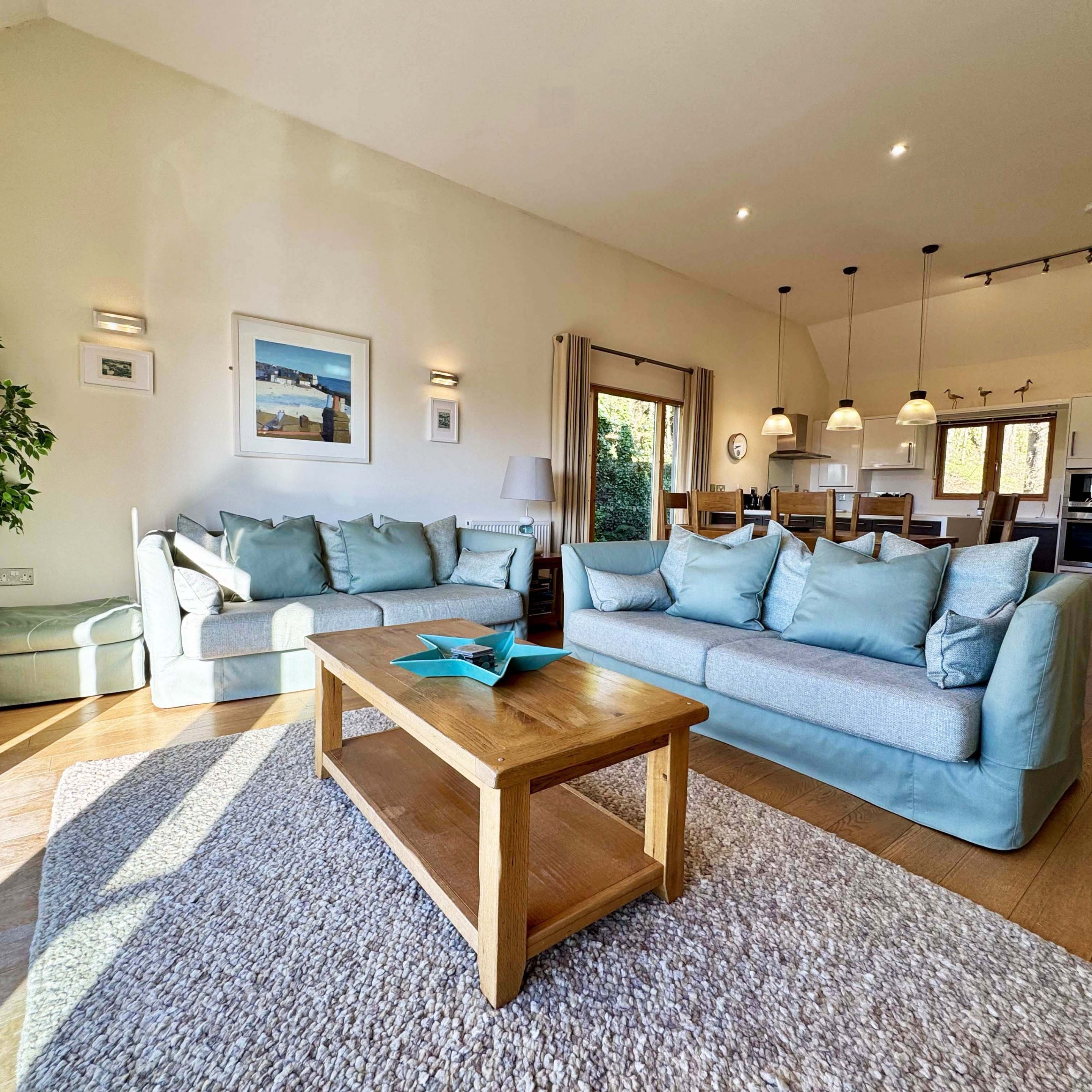 Modern open-plan living room with pastel sofas, wooden coffee table, and open kitchen in the background.