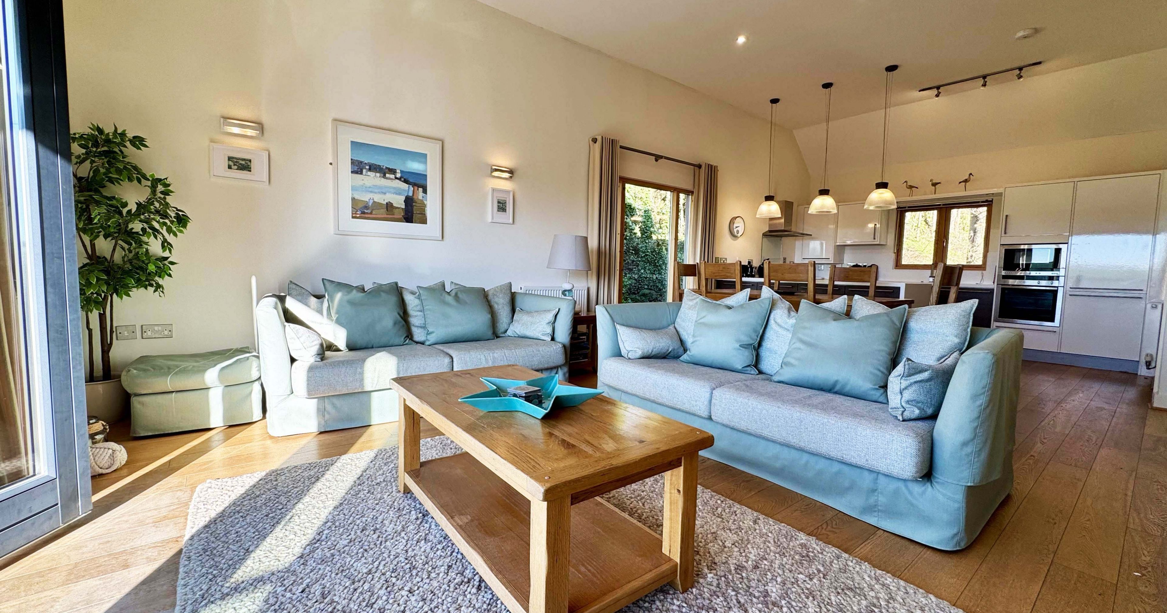 Modern open-plan living room with pastel sofas, wooden coffee table, and open kitchen in the background.