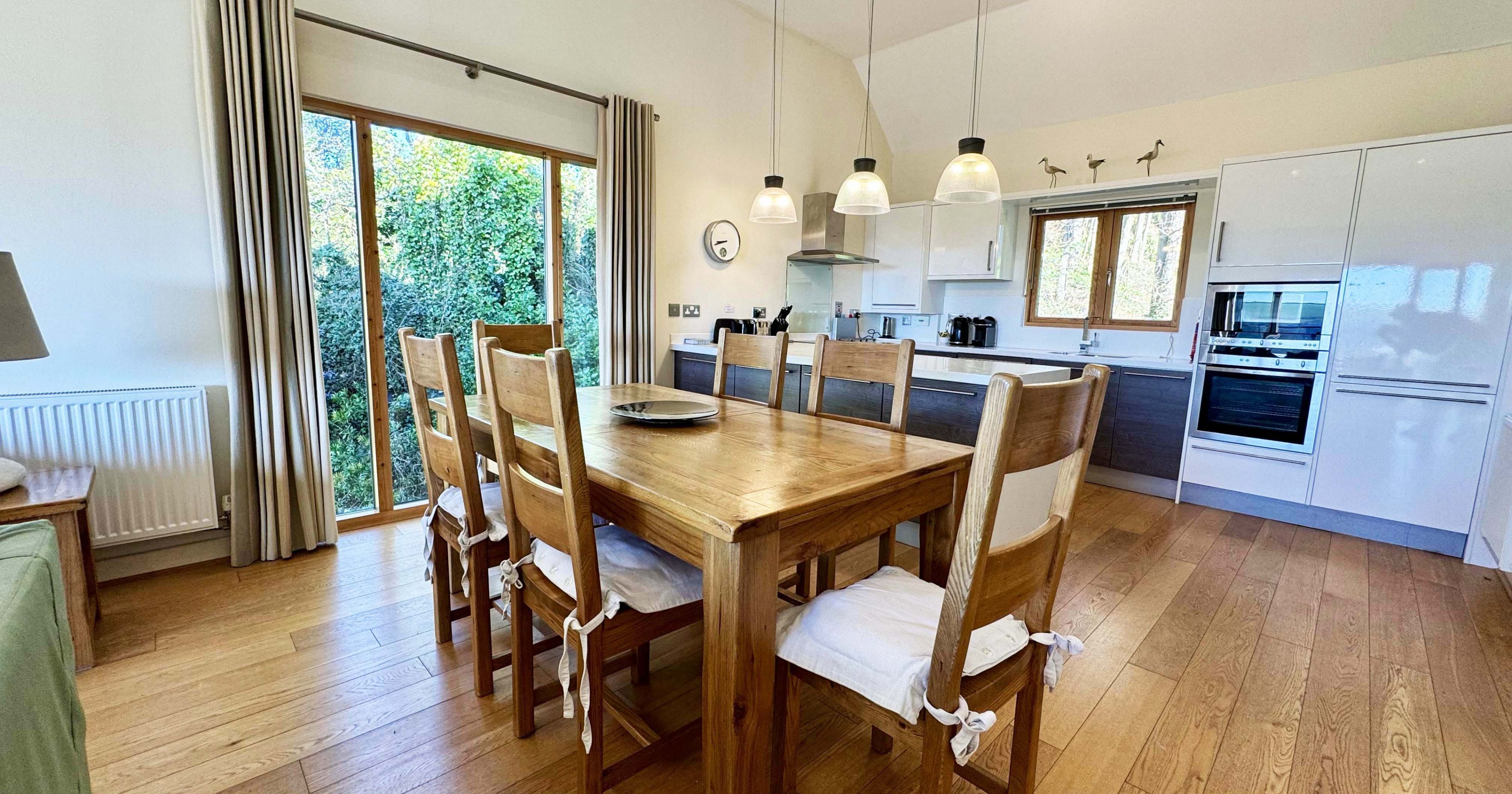 Modern kitchen and dining area with wooden table and chairs, pendant lights, and large window.