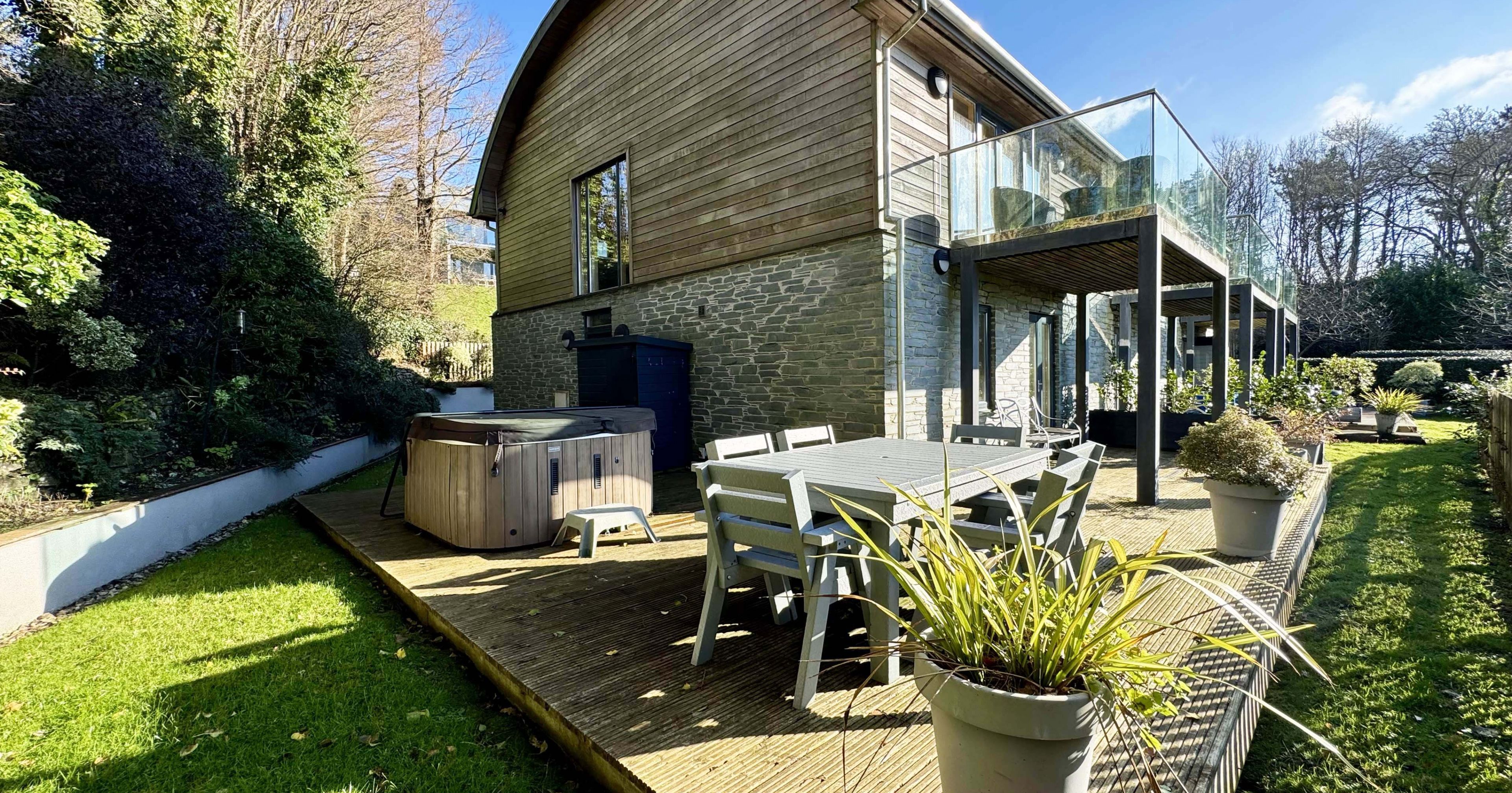 Modern house with wooden deck, outdoor dining area, and hot tub in a garden setting