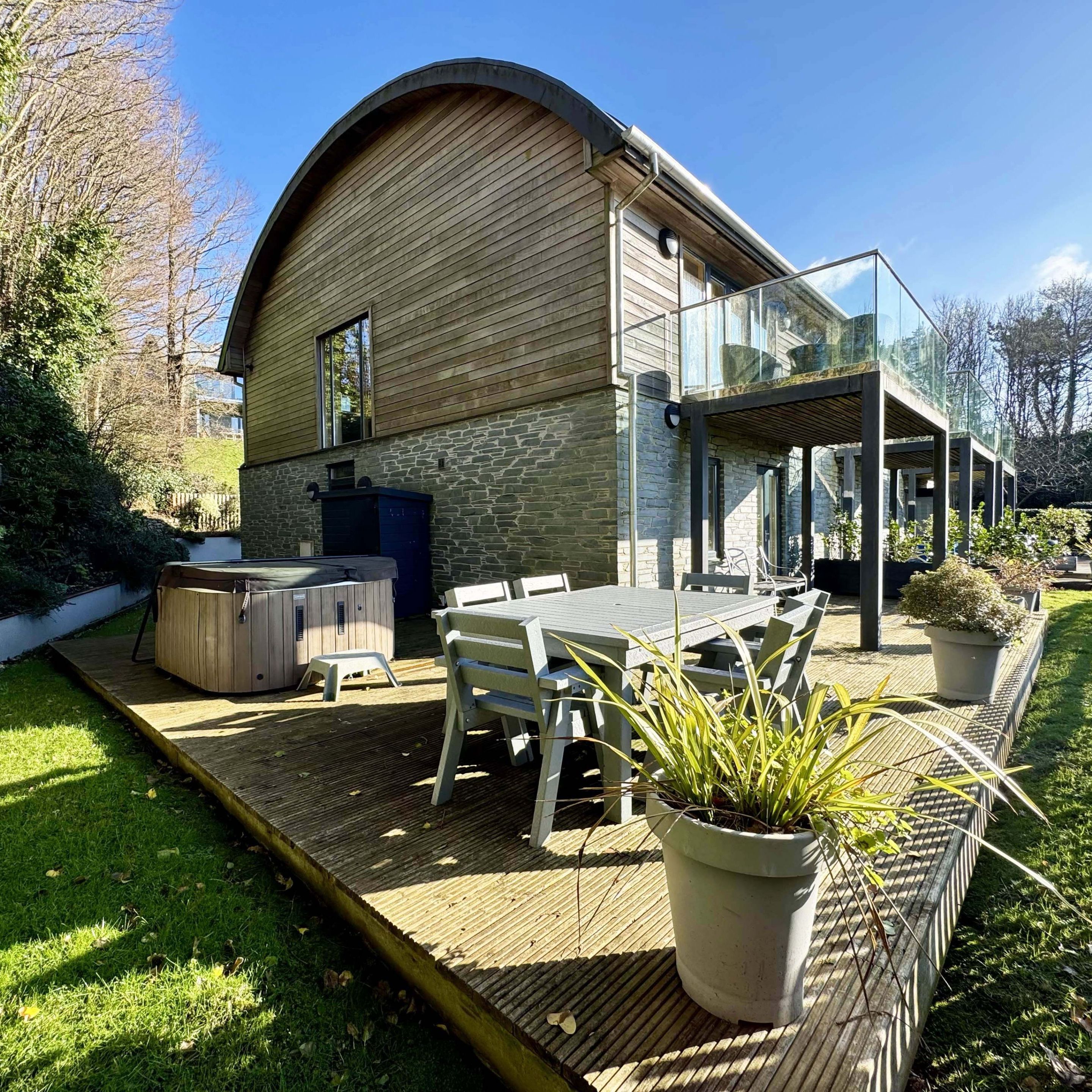 Modern house with wooden deck, outdoor dining area, and hot tub in a garden setting