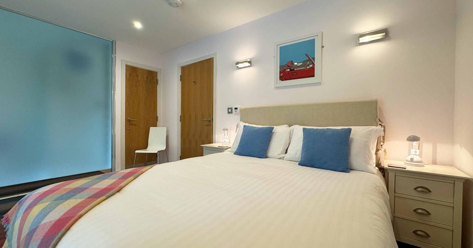 Modern bedroom with double bed, blue accent pillows, and bedside tables.