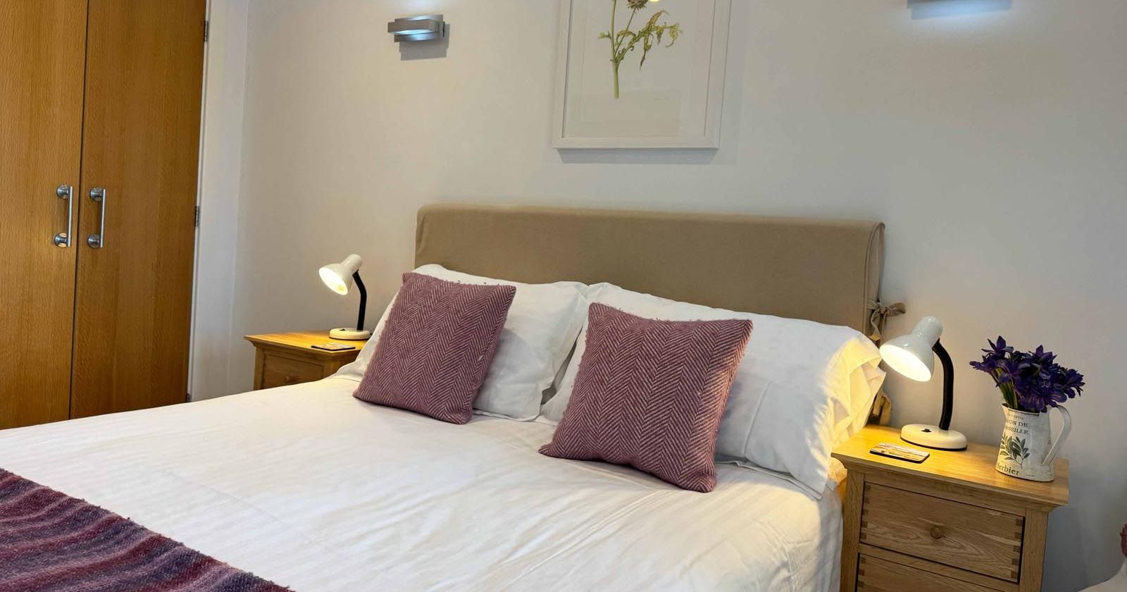 Cozy bedroom with double bed, pink pillows, bedside tables, and wall lights