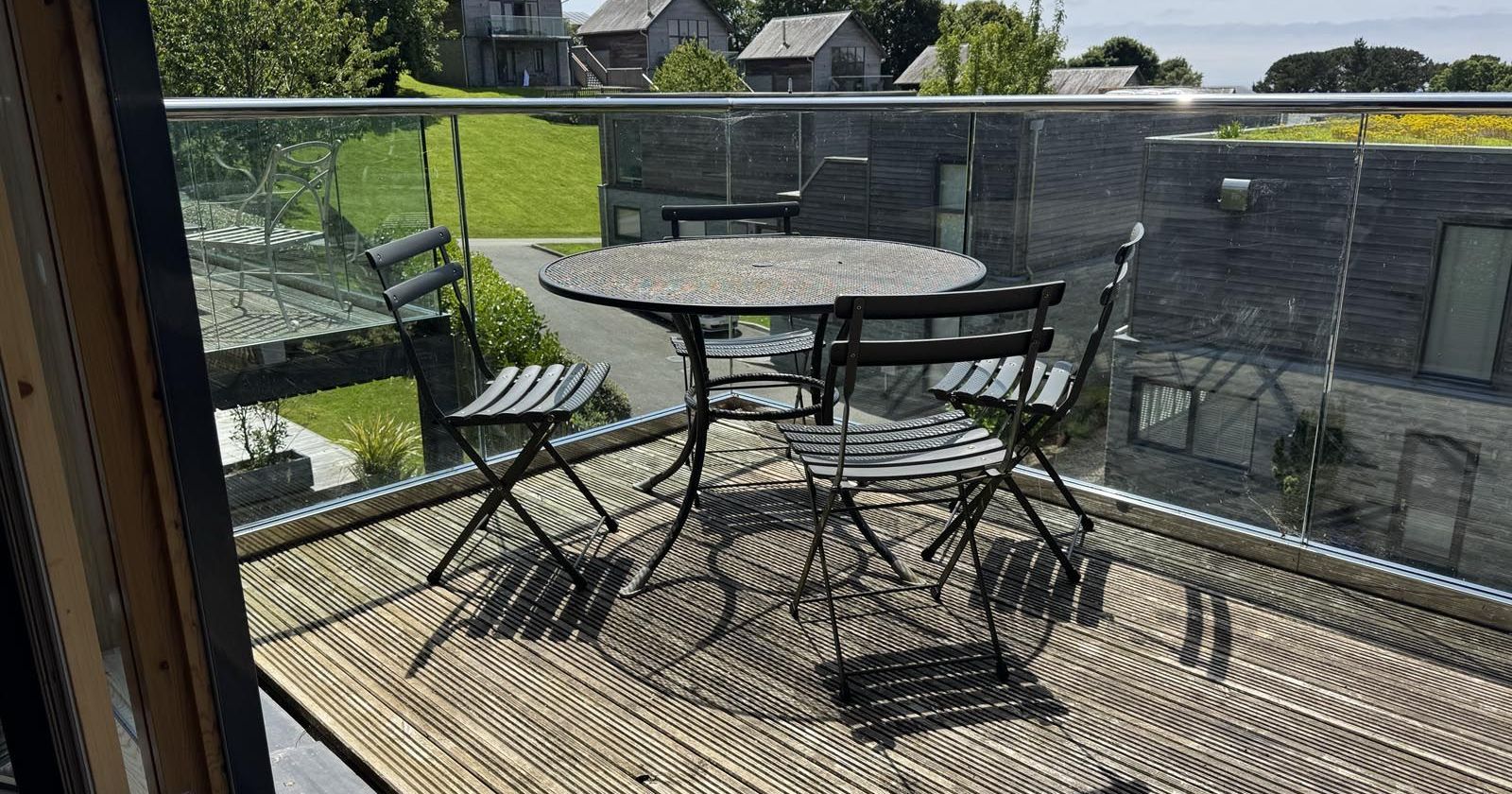 A balcony with a round table and four chairs overlooking a green lawn and modern houses.