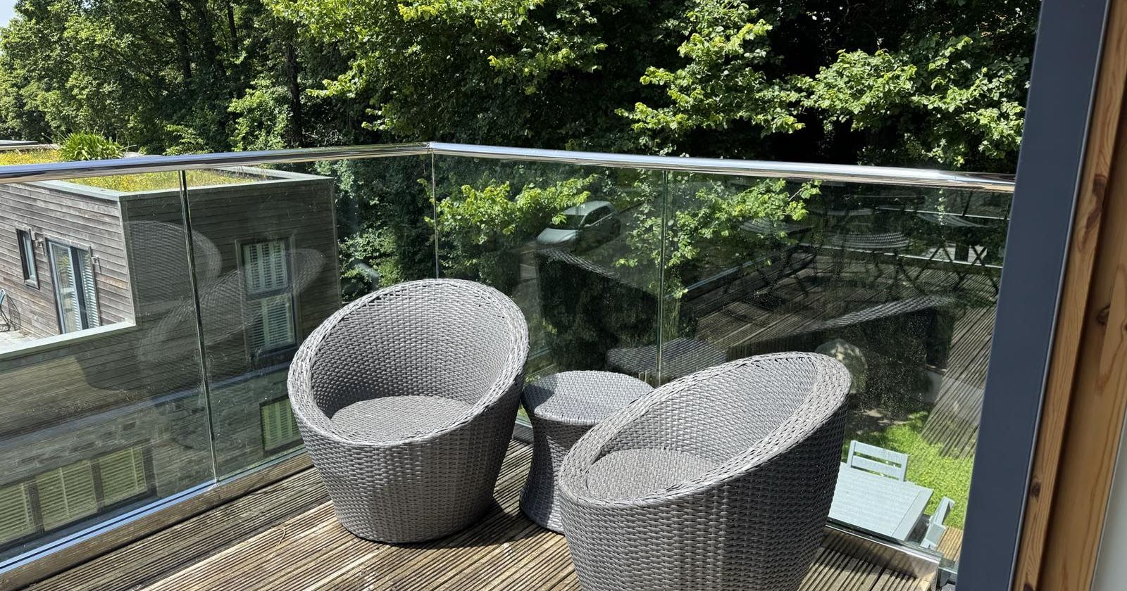 Two modern grey outdoor armchairs on a wooden deck balcony with glass balustrade