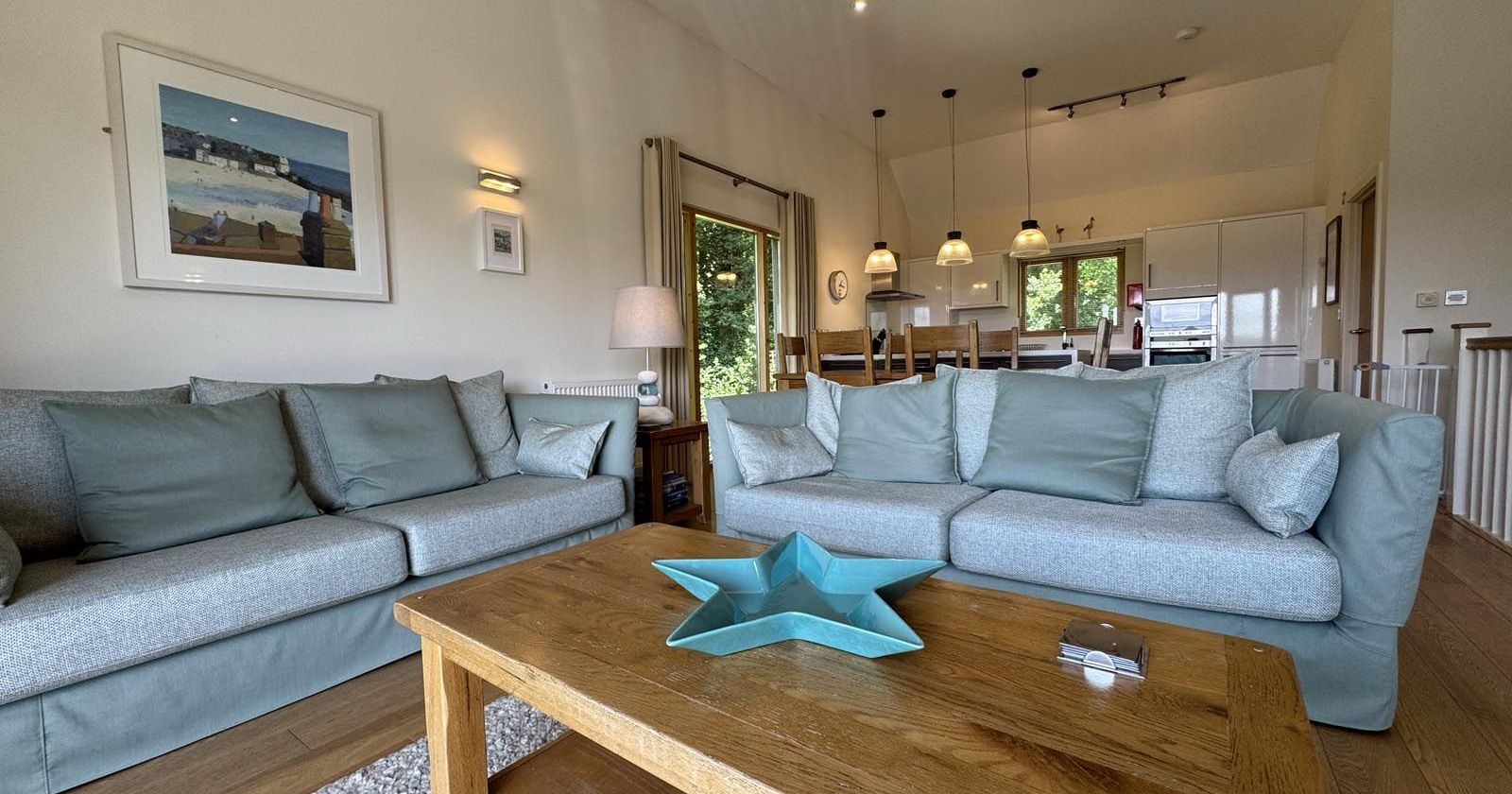 Modern living room with light blue sofas, wooden coffee table, and open kitchen in the background