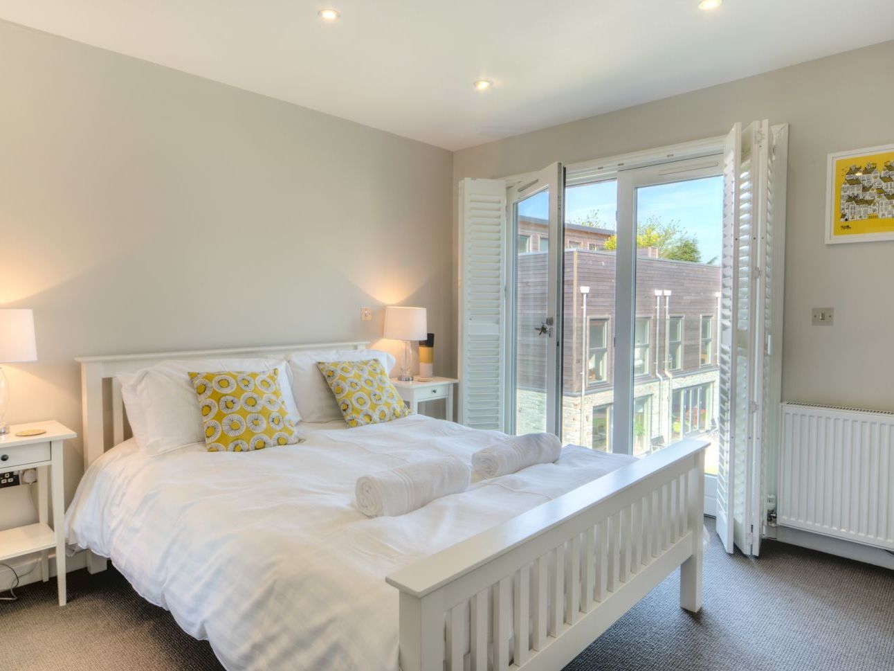 Bright modern bedroom with double bed, white linens, and open glass doors to a balcony.