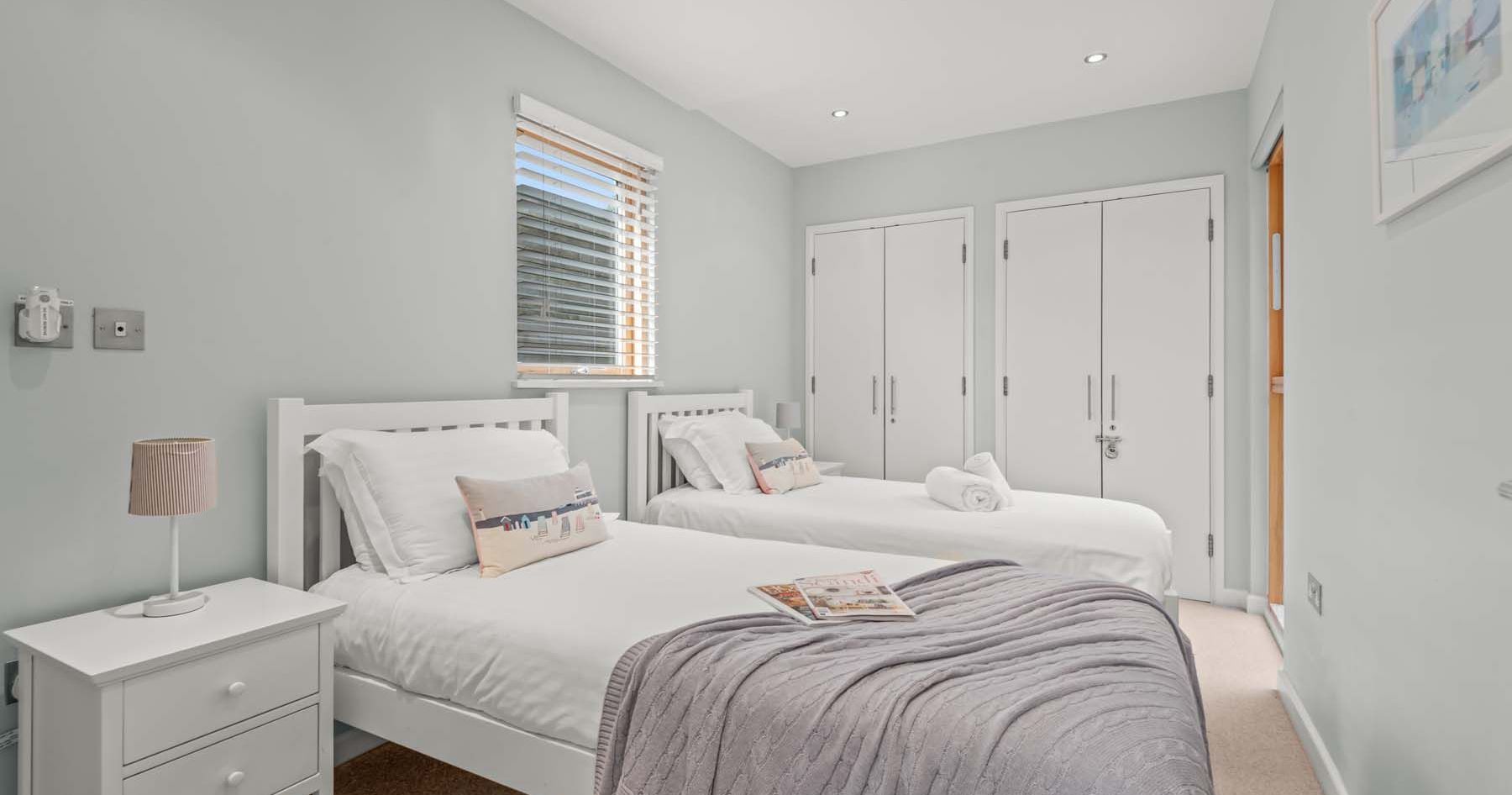 Modern bedroom with two single beds, white linens, and a nightstand.