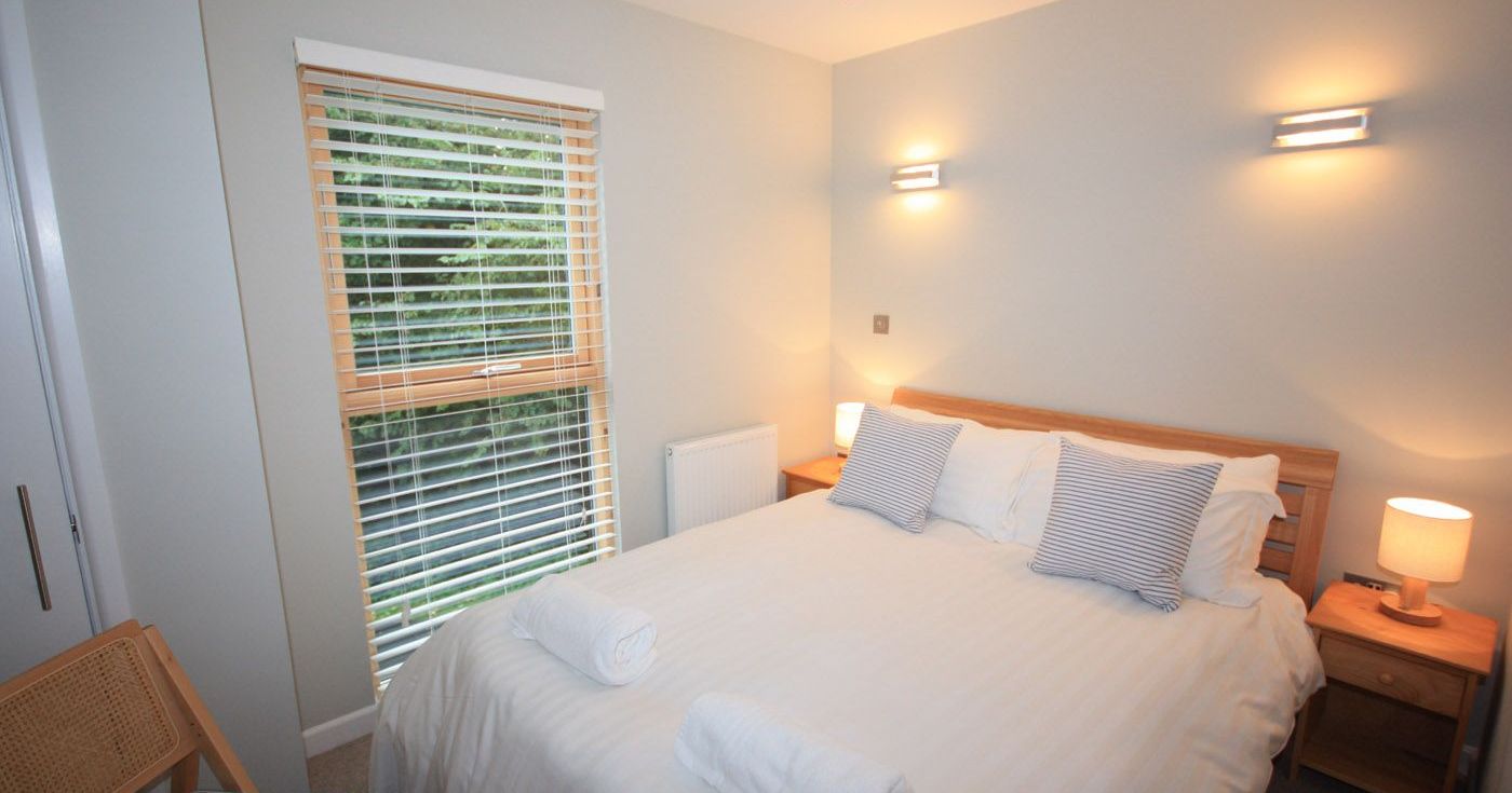 Modern bedroom with double bed, wooden blinds, and bedside lamps