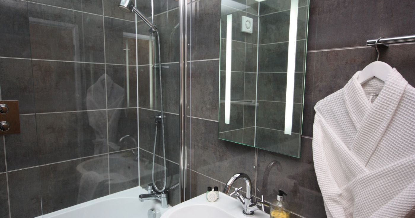 Modern bathroom with a robe hanging, illuminated mirror, and dark tile walls