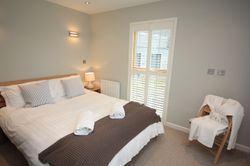 Modern bedroom with double bed, striped cushions, bedside lamp and chair with robe