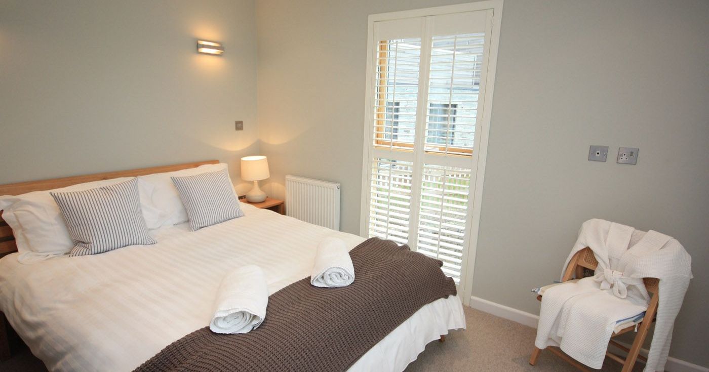 Modern bedroom with double bed, striped cushions, bedside lamp and chair with robe