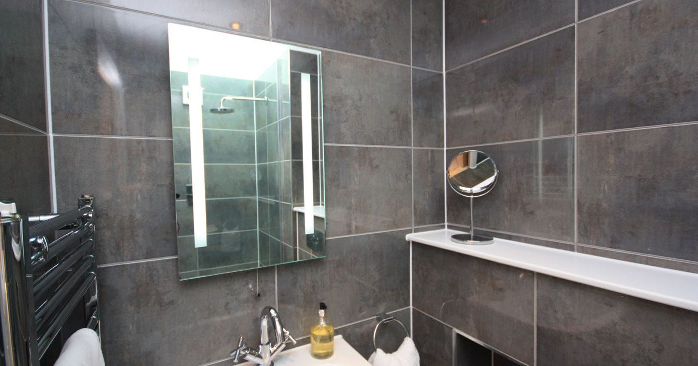 Modern bathroom with dark tile walls, illuminated mirror, and white sink