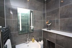 Modern bathroom with dark tile walls, illuminated mirror, and white sink