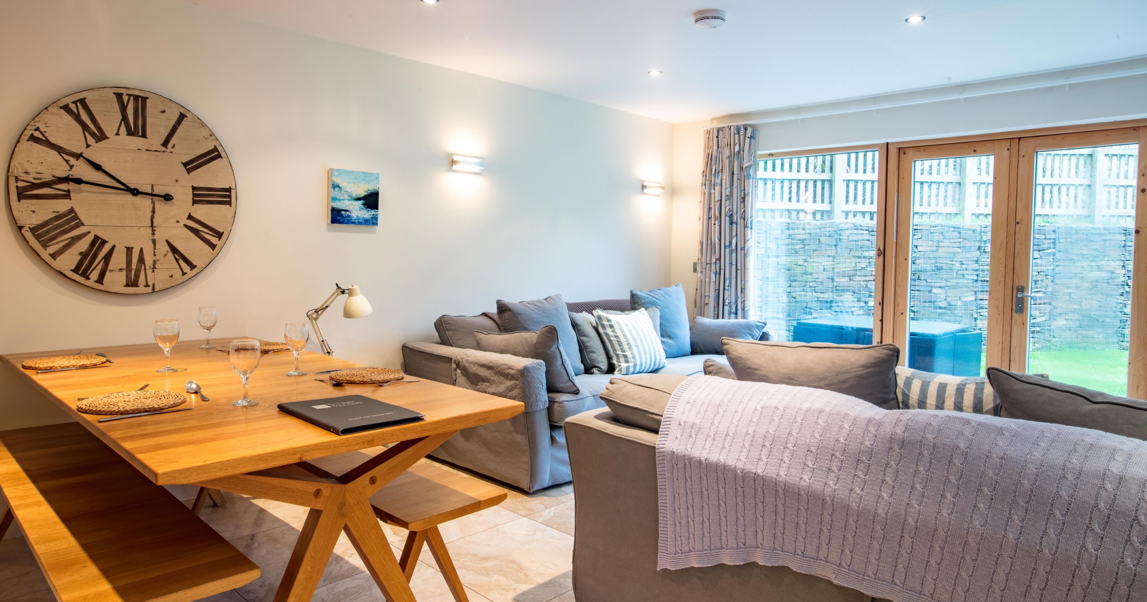 Modern open-plan living and dining area with grey sofas and wooden dining table.