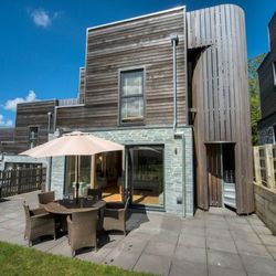 Modern house with wooden and stone exterior, patio with outdoor dining set and umbrella