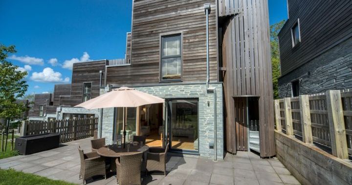 Modern house with wooden and stone exterior, patio with outdoor dining set and umbrella