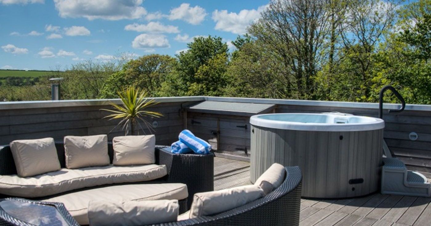 Outdoor deck with circular sofa and hot tub under blue sky