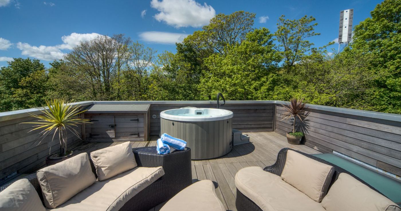 Outdoor deck with hot tub, cushioned seating, and trees in the background