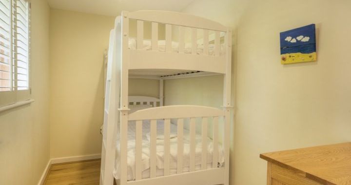 Small bedroom with white bunk bed, wooden floor, and dresser