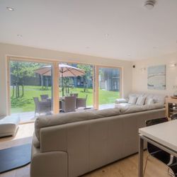 Modern open-plan living room and dining area with large windows overlooking a garden patio.