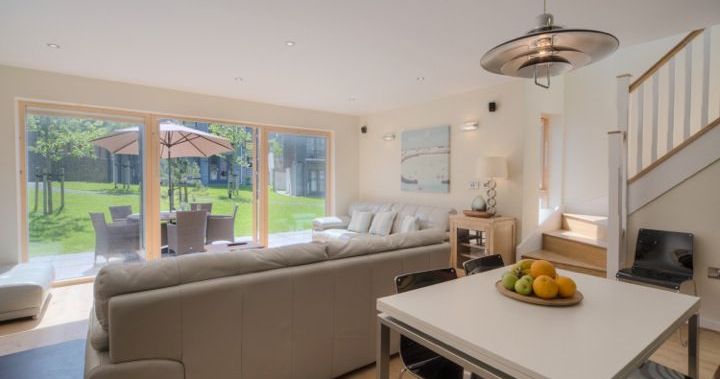 Modern open-plan living room and dining area with large windows overlooking a garden patio.