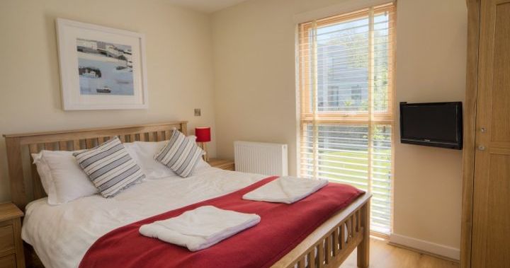 Modern bedroom with wooden furniture, a double bed with red blanket, and large window