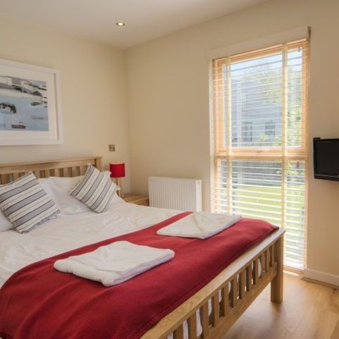 Modern bedroom with wooden furniture, a double bed with red blanket, and large window