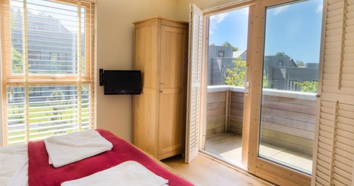 Bright bedroom with a double bed, red blanket, wardrobe, flat screen TV, and French doors opening to a small balcony.