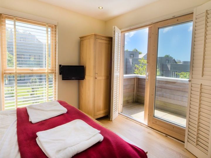 Bright bedroom with a double bed, red blanket, wardrobe, flat screen TV, and French doors opening to a small balcony.
