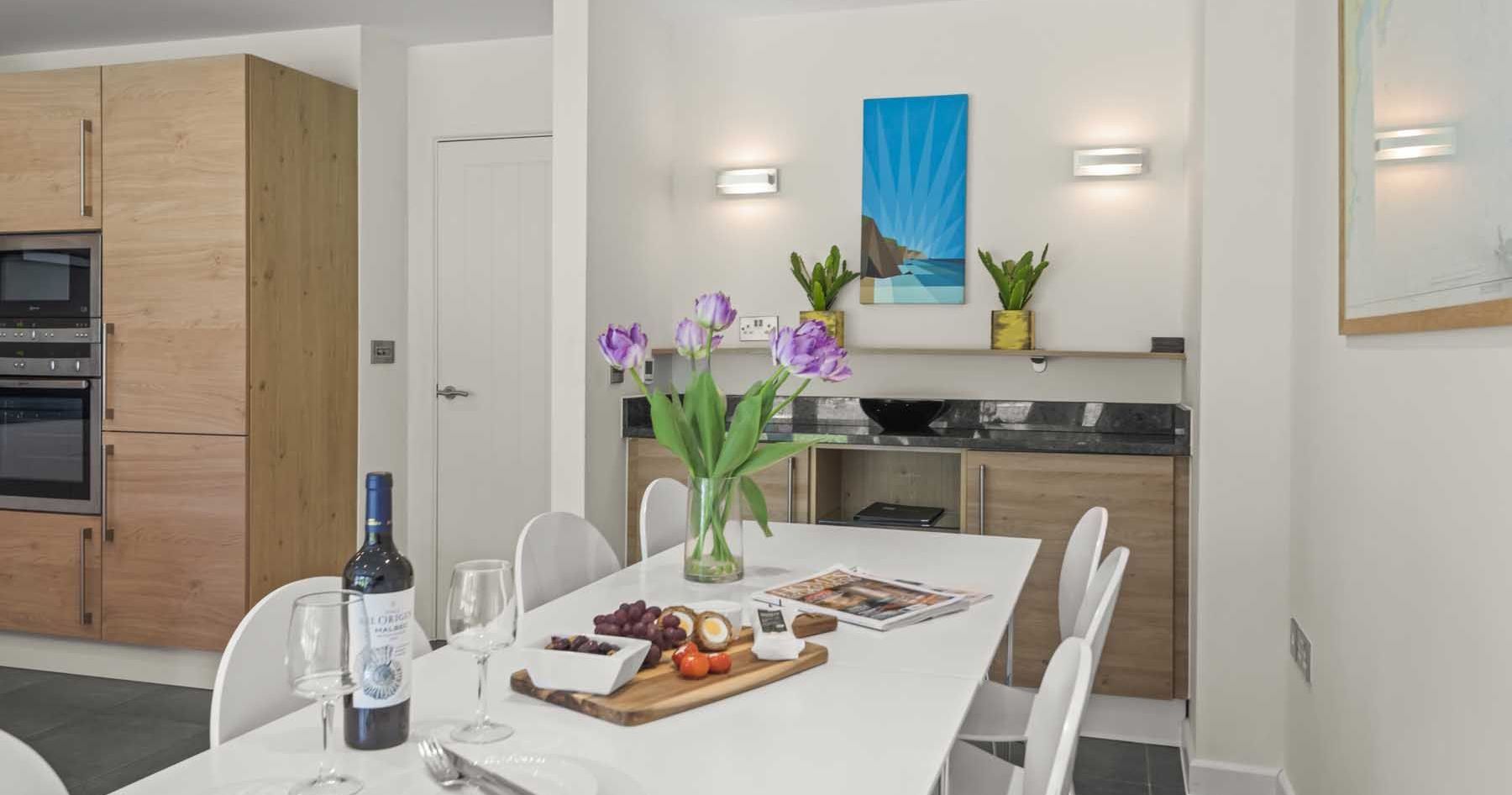 Modern kitchen with white dining table, wooden cabinets, and fresh flowers