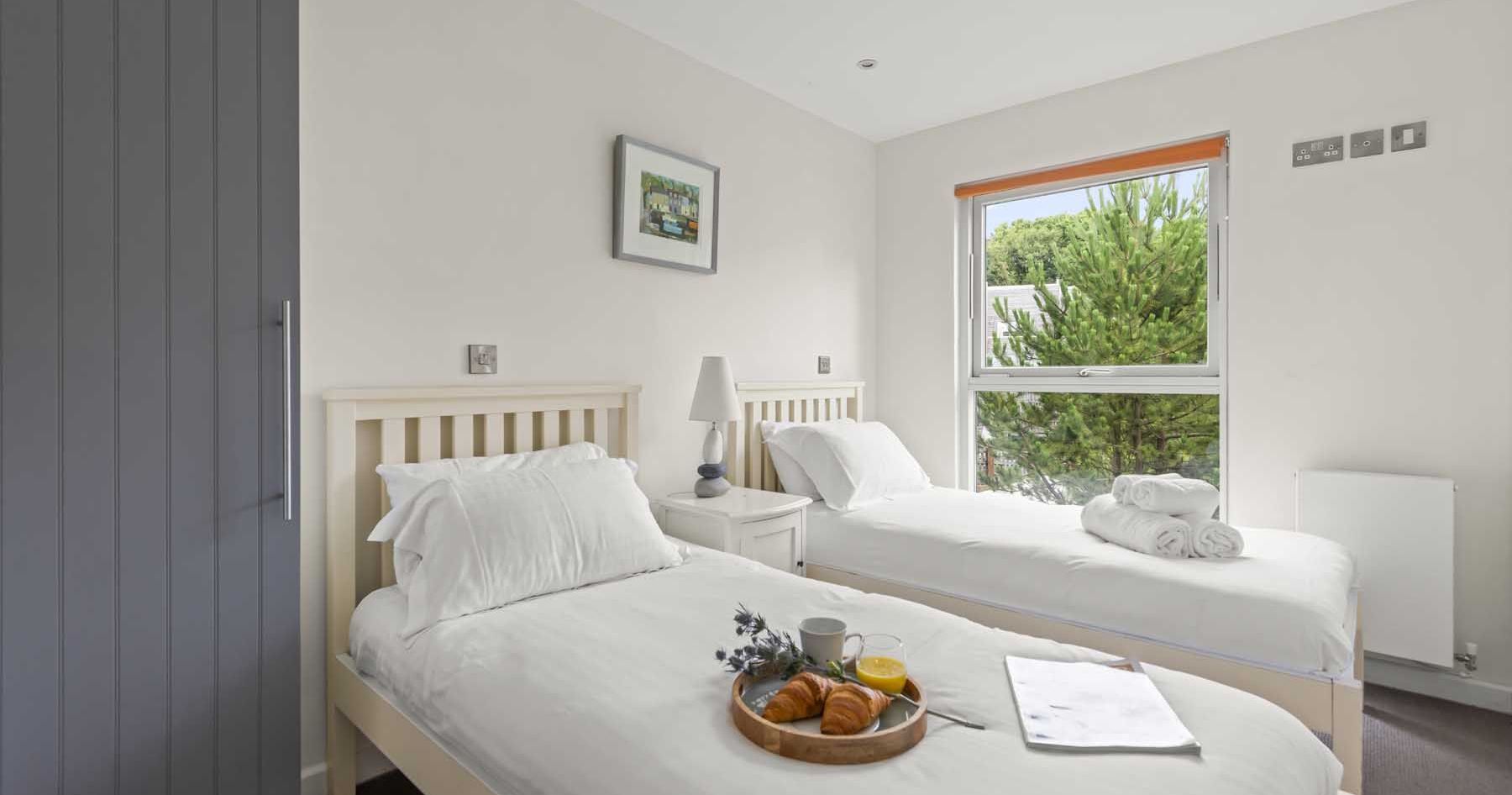 Bright bedroom with two single beds, a large window, and breakfast tray on one bed.