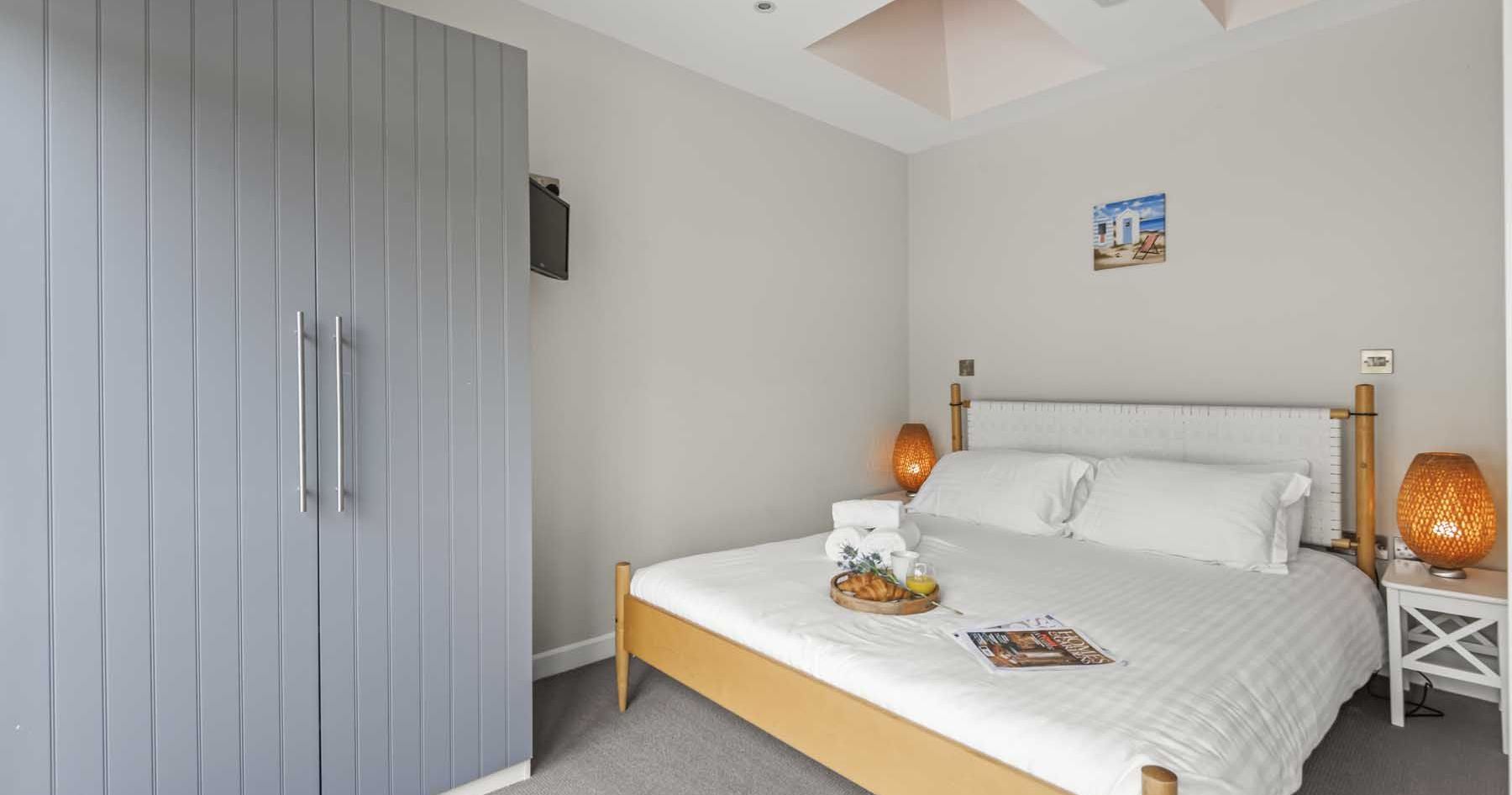 Bright and cozy bedroom with a double bed, two bedside tables with lamps, a blue wardrobe, and a skylight.