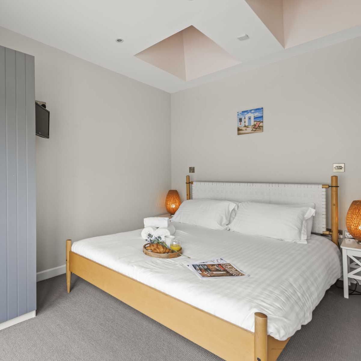 Bright and cozy bedroom with a double bed, two bedside tables with lamps, a blue wardrobe, and a skylight.