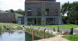 Modern house with wooden and stone exterior beside a pond and garden landscaping