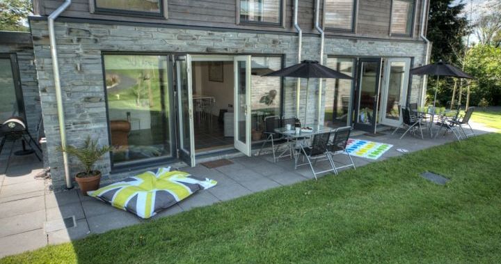 Modern patio with outdoor seating, open glass doors, umbrellas, and lawn games.