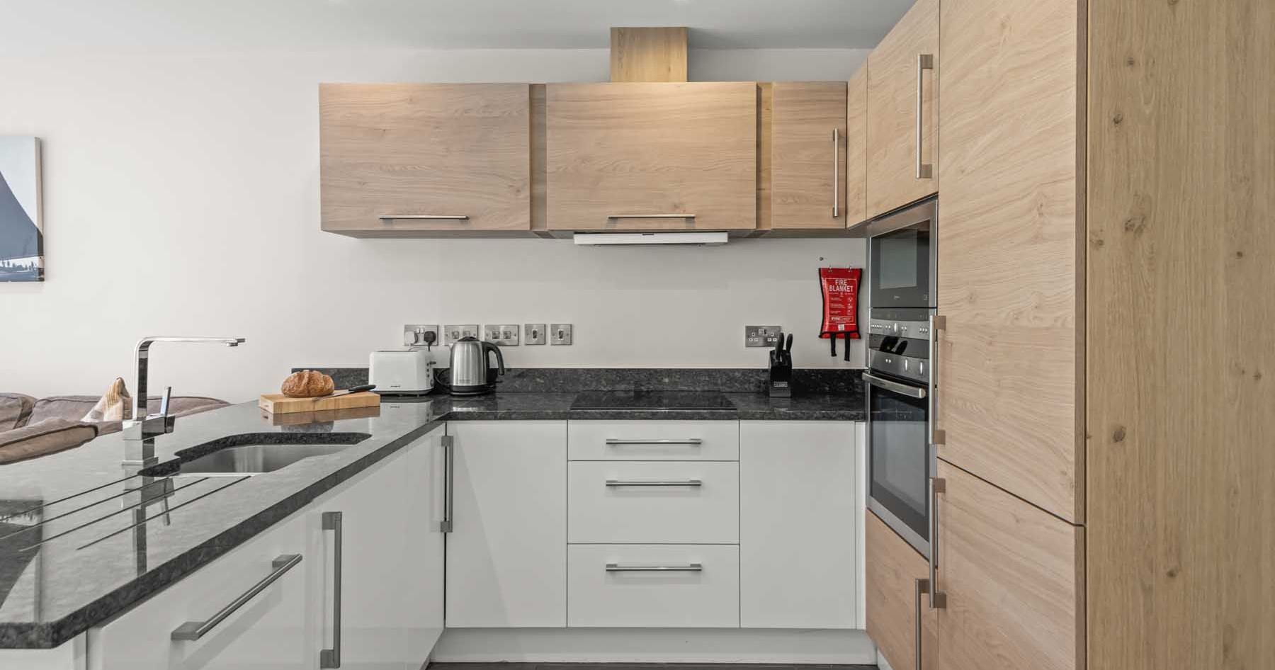 Modern kitchen with light wood cabinets, black countertops, and built-in appliances
